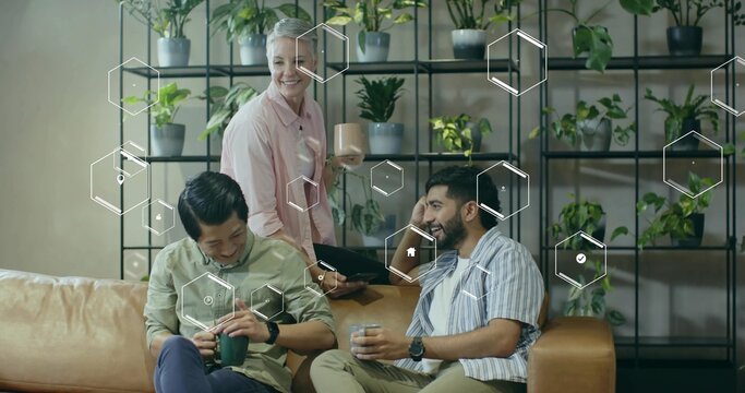 Reviewing tablet while holding mugs in office break area with leather couch, hexagonal graphics