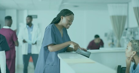 Obraz premium Pointing female nurse wearing navy scrubs consulting patient at reception desk, with tablet device