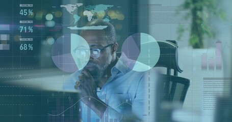 Studying male wearing glasses and shirt analyzing charts on computer monitor at office desk