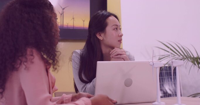 Discussing clean energy Chinese woman with colleague at office table, with turbine and solar models