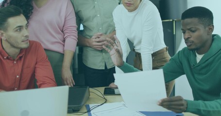 Gesturing man in green sweater reading document at office table with laptop, folder, copy space