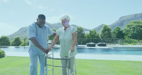 Helping caregiver in scrubs assisting senior patient in backyard, with metal walker, stethoscope