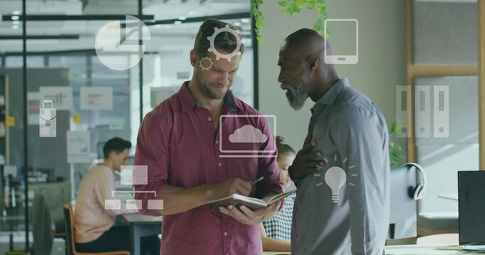Discussing colleagues in maroon and grey shirts taking notes in office, with notebook and monitor