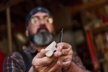 Man carving wood with a knife in workshop, craftsperson creating wooden figure, hobby and woodworking concept, artisan at work, handmade project, skill and creativity.