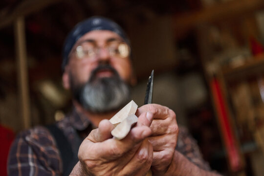 Man carving wood with a knife in workshop, craftsperson creating wooden figure, hobby and woodworking concept, artisan at work, handmade project, skill and creativity.