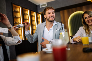 Friends enjoying drinks as man pays with card at restaurant