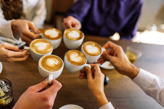 Group of friends cheering with coffee cups in cafe