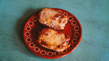 Dos porciones de molletes servidas en un plato de barro tradicional, sobre una mesa color turquesa. Presentación sencilla y casera.