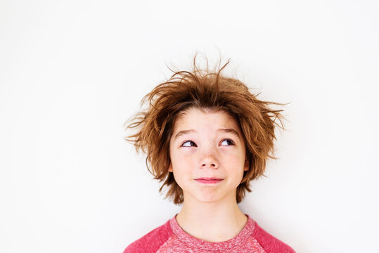 Close-up portrait of a boy with messy hair standing in front of a white background glancing sideways
