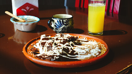Plato de enmoladas cubiertas con crema y queso, acompañado de jugo y café sobre una mesa de...