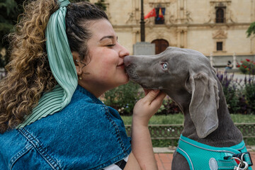 Woman kissing her weimaraner dog in a city park