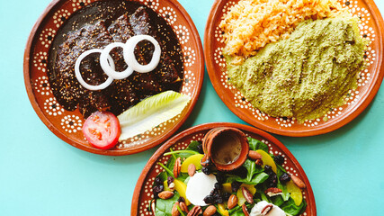 Vista aérea de mesa con tres platillos mexicanos coloridos: enchiladas de mole, pollo en salsa...