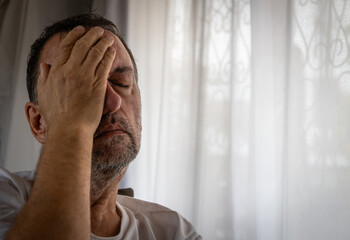 Tired middle-aged man covering his face with hand feeling stressed at home.
