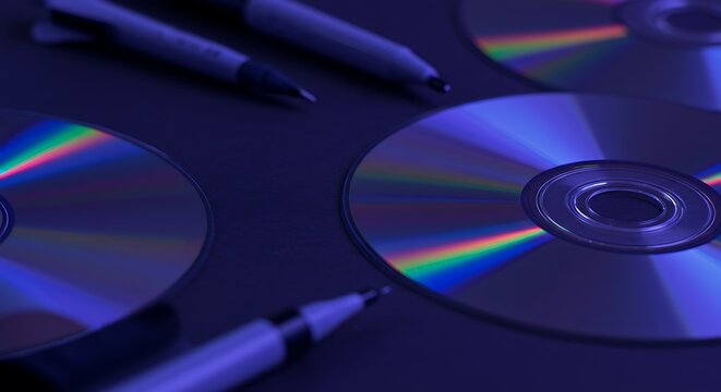 Close-up of optical discs with accompanying pens in cool-toned, selective focus composition
