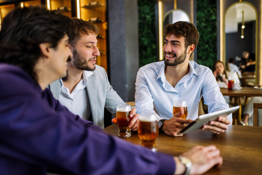 Colleagues discussing work over beer in restaurant - Powered by Adobe