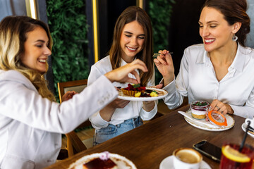 Three women enjoying cakes in restaurant after shopping