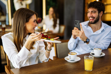 Boyfriend taking photo of his girlfriend eating cake in restaurant