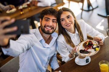 Couple taking selfie while eating cake in restaurant