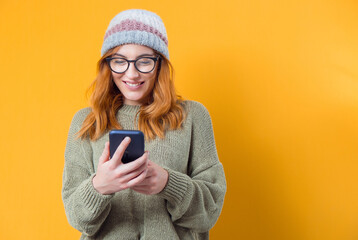 Beautiful young woman browse on smartphone, isolated on yellow background. Trendy girl holding mobile phone