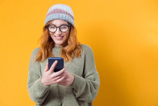Beautiful young woman browse on smartphone, isolated on yellow background. Trendy girl holding mobile phone