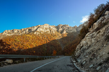 Mountain road with protective netting against rockfalls, showing autumn forest and rocky cliffs...