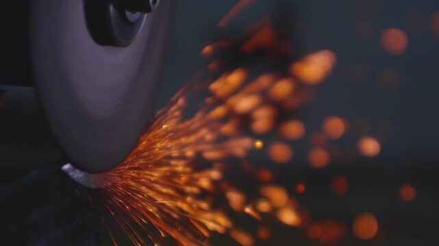 An angle grinder sharpens a steel impact tool. Sparks fly from the power tool blade. Close-up of spinning disc in motion, creating dynamic shower of fire. Angle grinder machine cutting iron in factory