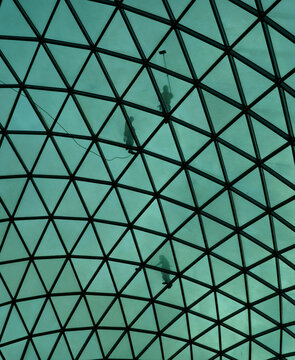 Silhouetted workers clean a vast, geometric glass dome, its triangular panels glowing teal from the light above.