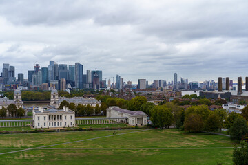 Obraz premium Greenwich Park and Old Royal Naval College, with the River Thames and modern Canary Wharf skyline under an overcast London sky.
