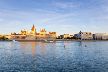 Fototapeta premium Unrecognizable people on paddle boards on the Danube river and the 1902 Gothic Revival style Parliament seen during the late afternoon golden hour, Budapest, Hungary