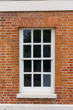 A white-framed window with multiple panes set in a red brick wall, featuring an arched brick lintel with white markings and a lower white section with peeling paint.