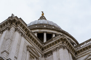 St. Paul's Cathedral's majestic dome and golden finial, seen from below, highlight intricate classical architecture, columns, and stone carvings against a light sky. © Jarrod