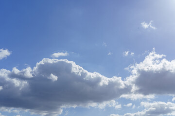 Partly cloudy blue sky with white and gray clouds, and a bright sun flare.