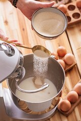 Hands gracefully pour sugar into a stand mixer filled with milk, preparing to create Romanian...