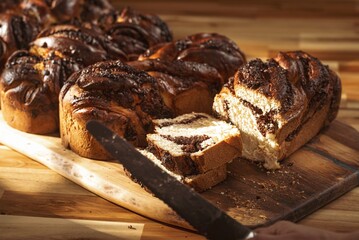 Cozonac, a traditional Romanian sweet bread, is being sliced on a wooden board. This festive treat blends various cultural influences, showcasing rich flavors and textures