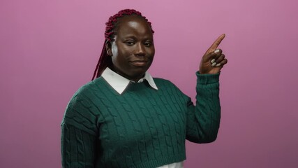 Woman in a green sweater with braided hair pointing at something against a pink background, suggesting direction or attention in a studio setting. - Powered by Adobe