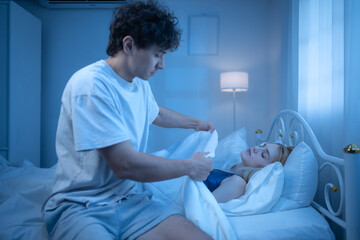 Obraz premium A man sits beside a sleeping woman suffering from a cold in a dimly lit bedroom
