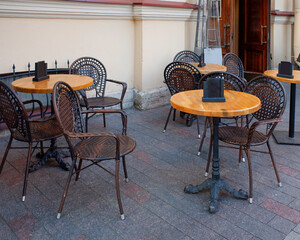 Outdoor seating area of a cafe with round wooden tables and wicker chairs arranged on a stone-tiled patio.