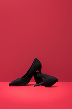 Black suede high-heeled shoes on red background