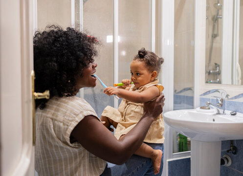 Mother and daughter brushing teeth together at home - Powered by Adobe