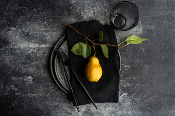 Minimalist table setting with pear on dark surface
