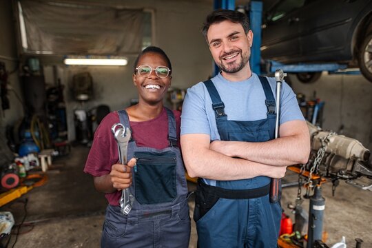 Mechanics smiling and holding wrenches in auto repair shop