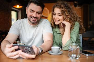 Couple enjoying coffee and looking at smartphone in cafe