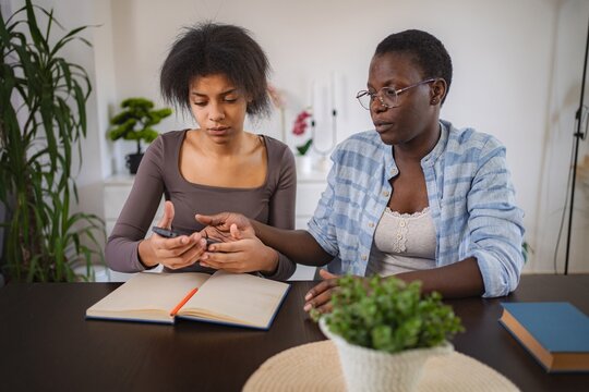 Two Young Women Collaborating on a Project Using a Smartphone and Notebook at Home