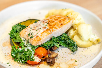 Tasty grilled salmon steak with vegetables and mashed potatoes served on light wooden table, closeup.