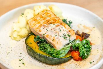 Tasty grilled salmon steak with vegetables and mashed potatoes served on light wooden table, closeup.