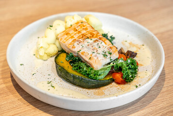 Tasty grilled salmon steak with vegetables and mashed potatoes served on light wooden table, closeup.