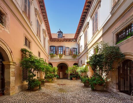 an architectural courtyard with an archway historic buildings and well tended plants creates the atmosphere of an old european city useful for projects about travel and architecture - Powered by Adobe