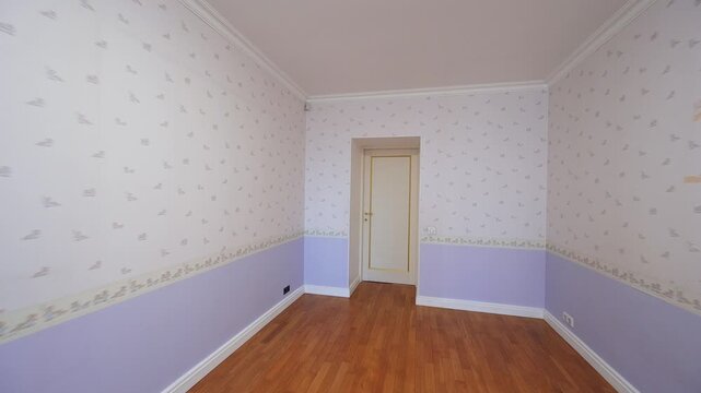 An empty room with hardwood floors, floral wallpaper and a white door.