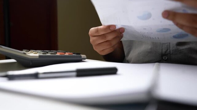 Person using a calculator with a notepad and pen on a desk shot - Powered by Adobe