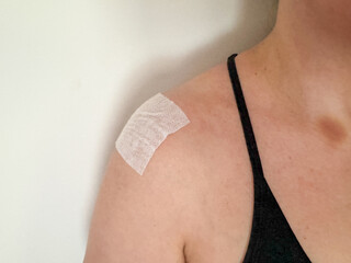 Injury recovery concept showing female shoulder with medical patch on deltoid muscle after training or inflammation, physical therapy background